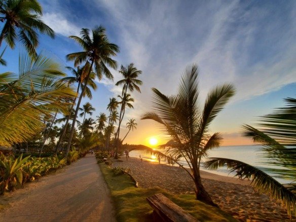 Sunset over Playa Bonita beach with palm trees, sandy shoreline, and oceanfront walking path in Las Terrenas, Dominican Republic